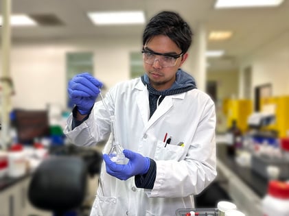 Chemist wearing a white lab coat adding analyte to a flask in a OTC and cosmetic testing laboratory.