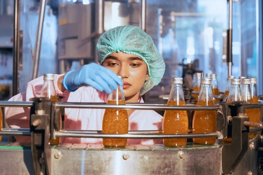 Food scientist wearing personal protective equipment observing a bottled beverage on a food packaging line.