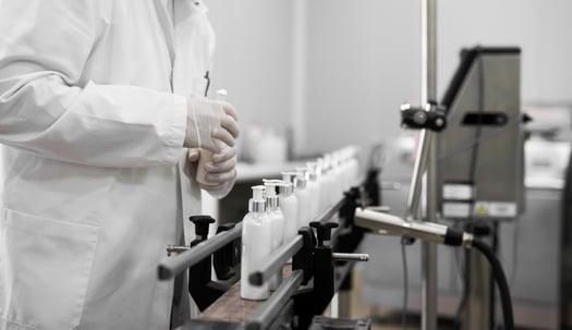 Cosmetics worker in lab coat taking bottle of liquid product from assembly line.
