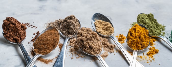 Various spices in metal spoons on a countertop.