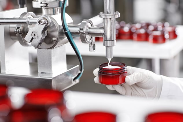 Machine dispensing cream into small jar in cosmetic manufacturing facility