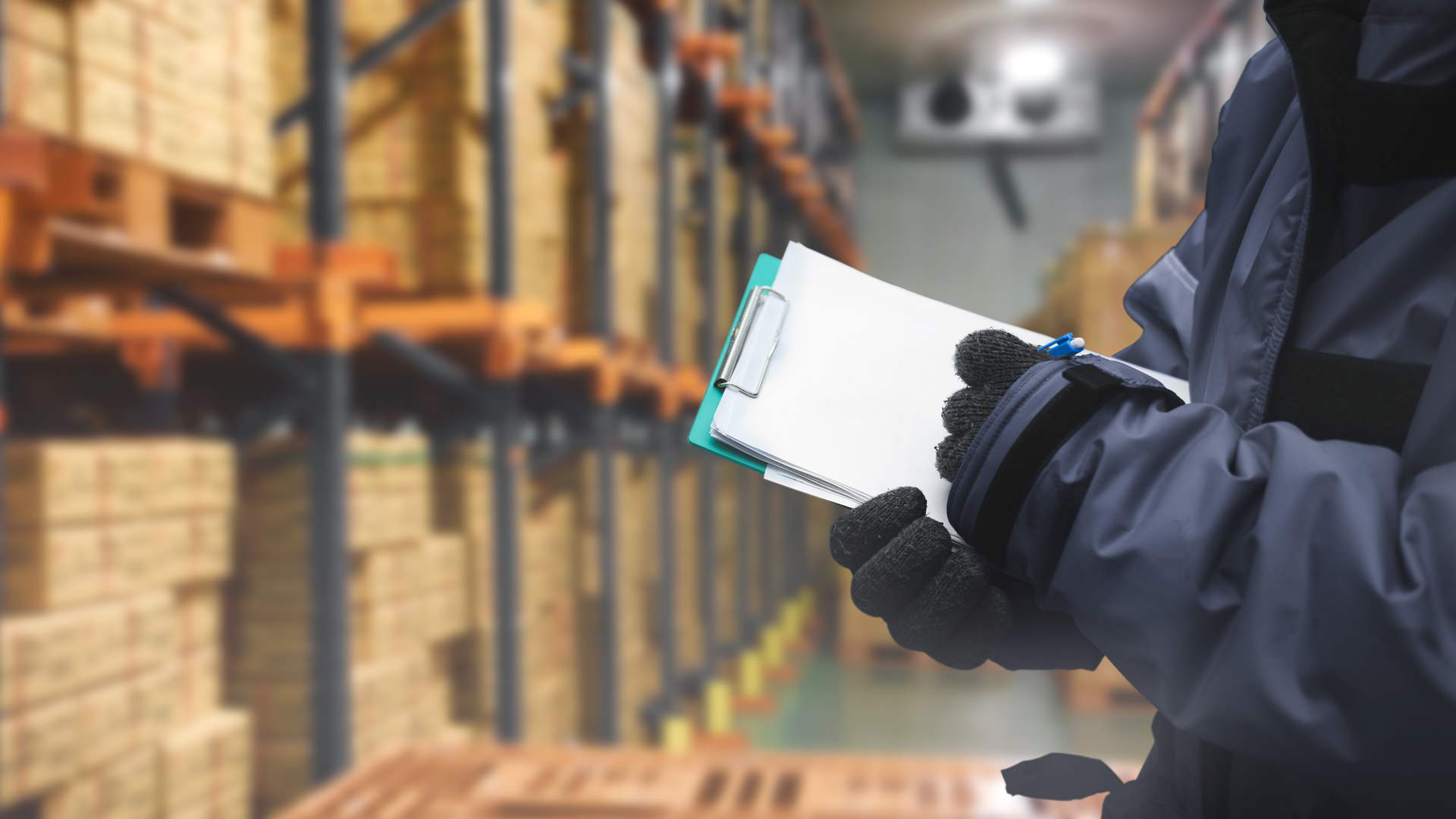 Worker with clipboard in warehouse examining cases of product. 