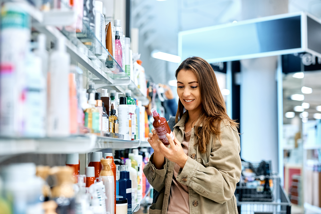 Woman examining cosmetic product label claim in retail store. 